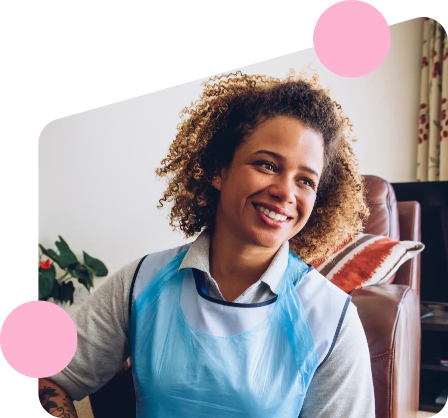 A smiling adult care worker wearing a blue apron in a community environment.